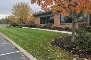 lawn winterization Lancaster Ohio commercial office grounds with mowed turf, mulched beds, and fall leaves along a parking lot curb (AI-generated image)